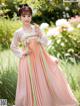 A woman in a pink and green hanbok standing in a garden.