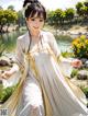 A woman in a white and yellow dress standing in front of a pond.