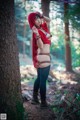 A woman in a red hooded outfit standing next to a tree.