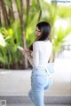 A woman in jeans and a white shirt is looking at her phone.